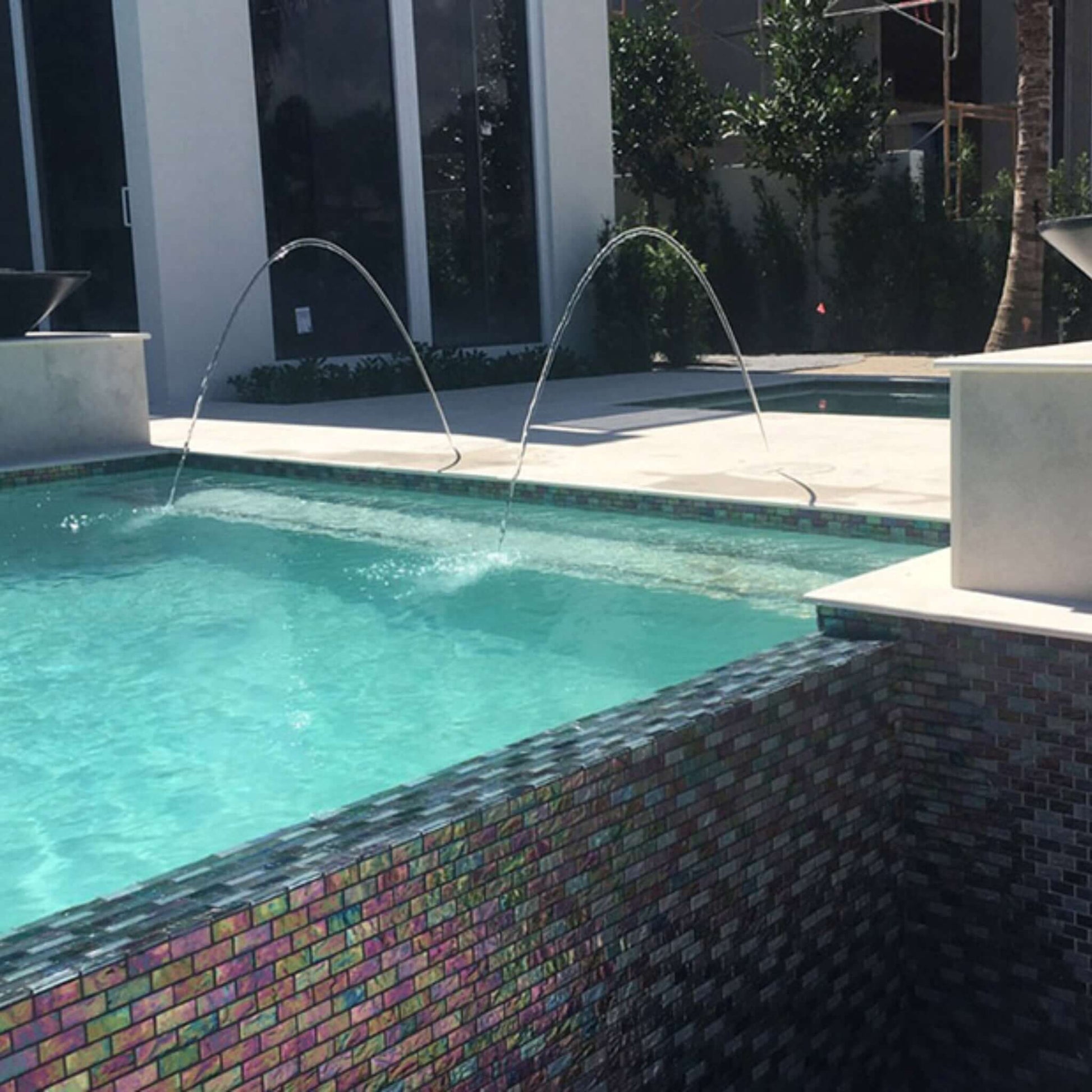 Elegant swimming pool featuring glass tile with water features, showcasing modern design and luxurious aesthetics.