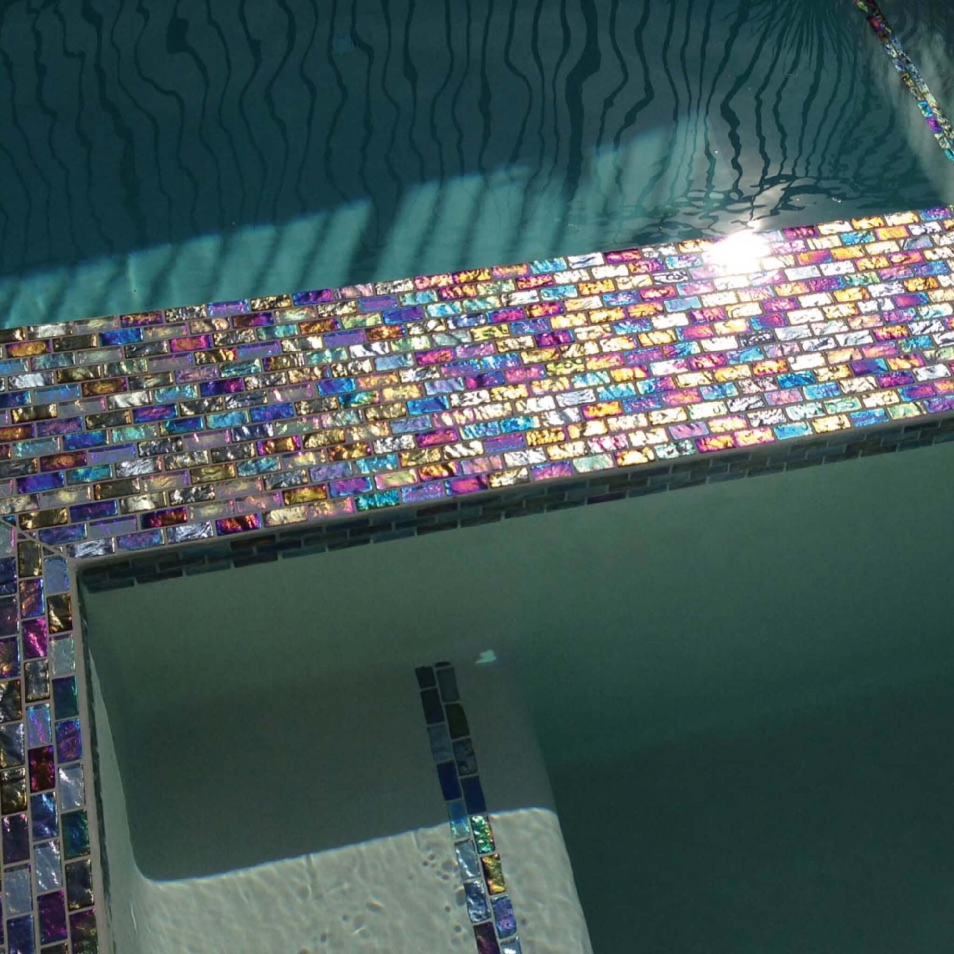 Colorful mosaic glass tiles in a pool design, reflecting sunlight. Ideal for modern aesthetics, enhancing pool appeal.