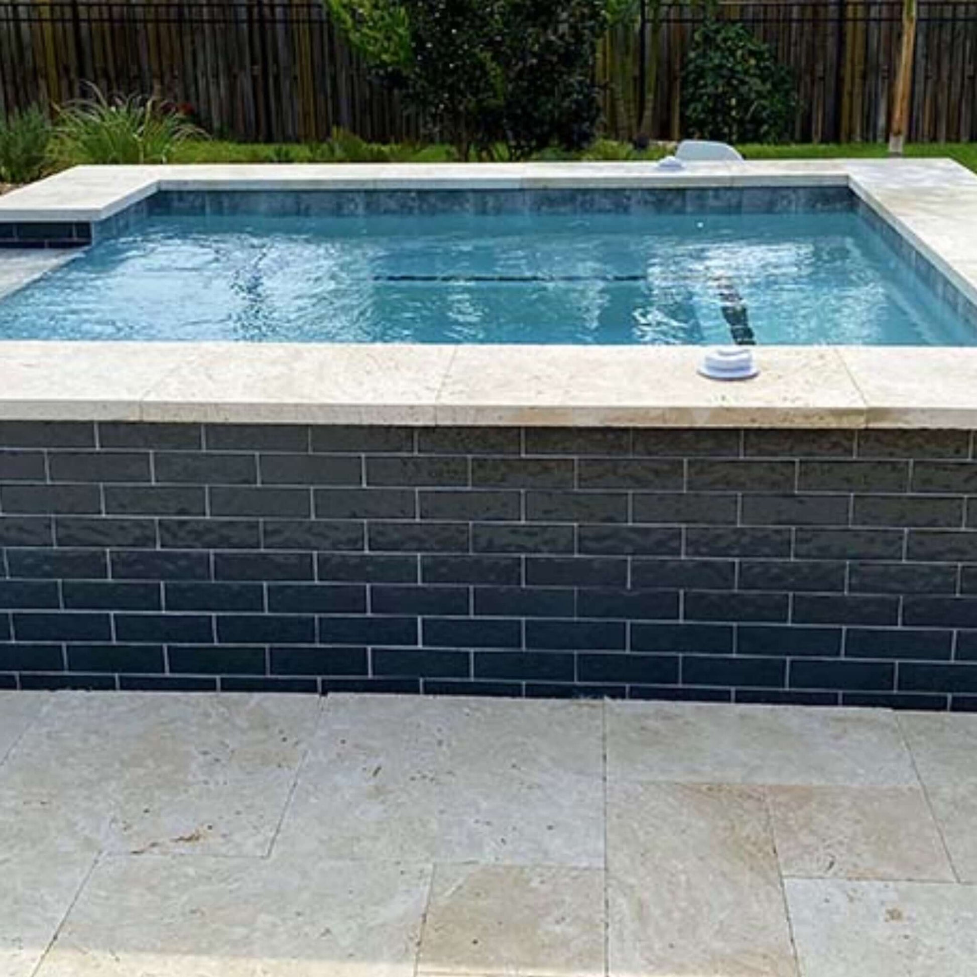 Modern pool design featuring sleek black glass tiles and light stone coping, perfect for stylish outdoor spaces.
