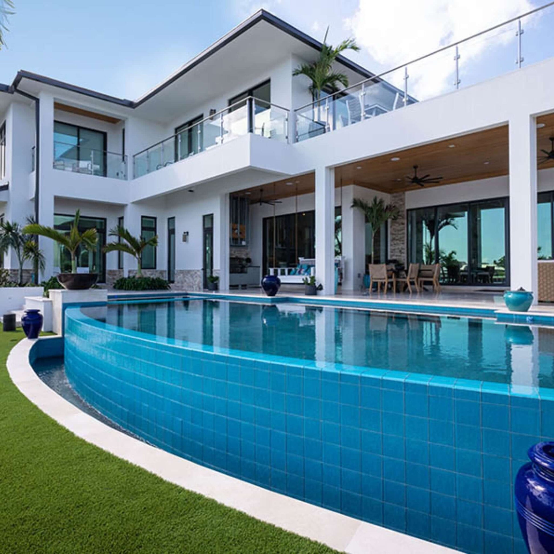 Luxury pool view with turquoise tiles and elegant house design featuring modern architecture and lush landscaping.