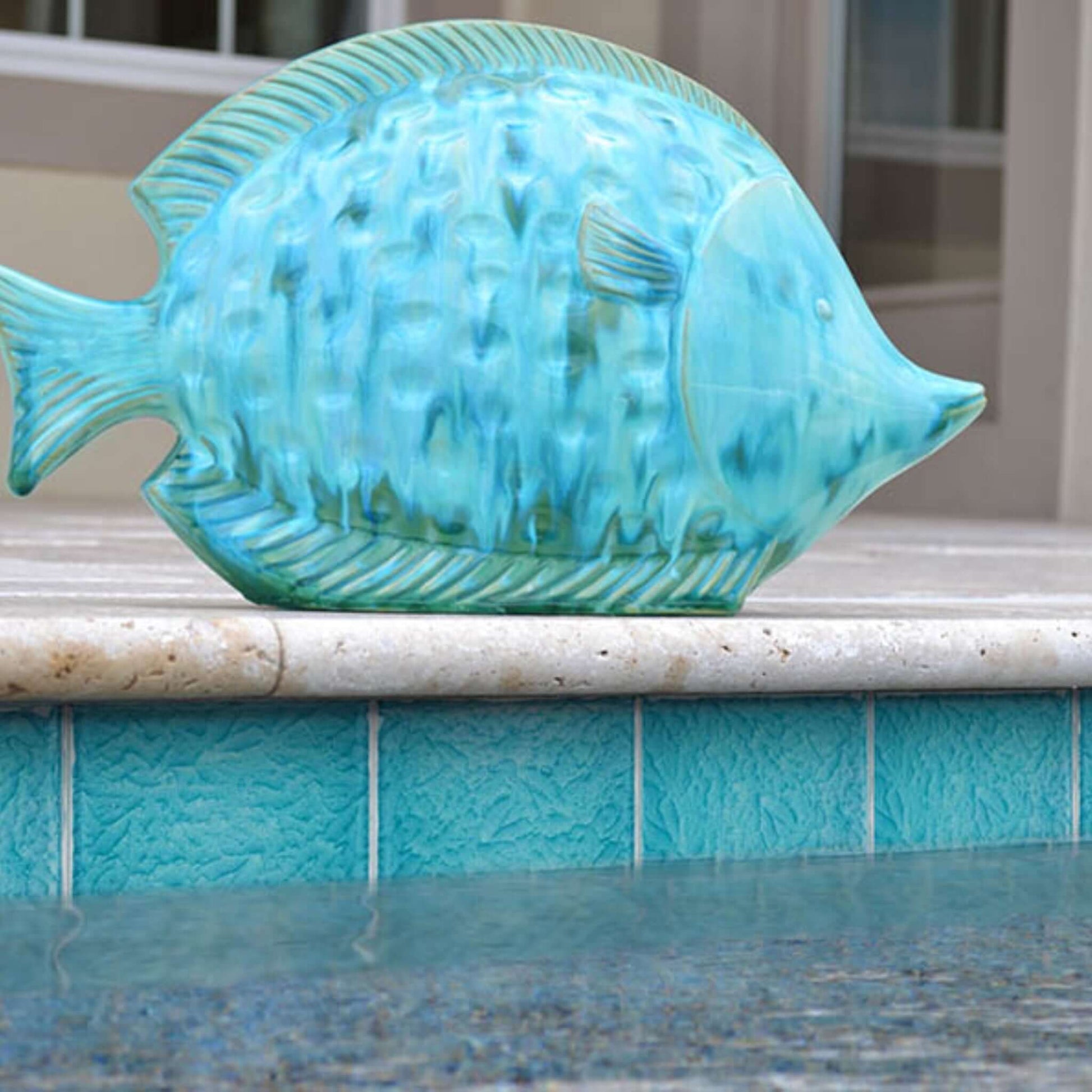 Turquoise ceramic fish sculpture beside a turquoise tiled pool, adding a vibrant decorative touch to the backyard.