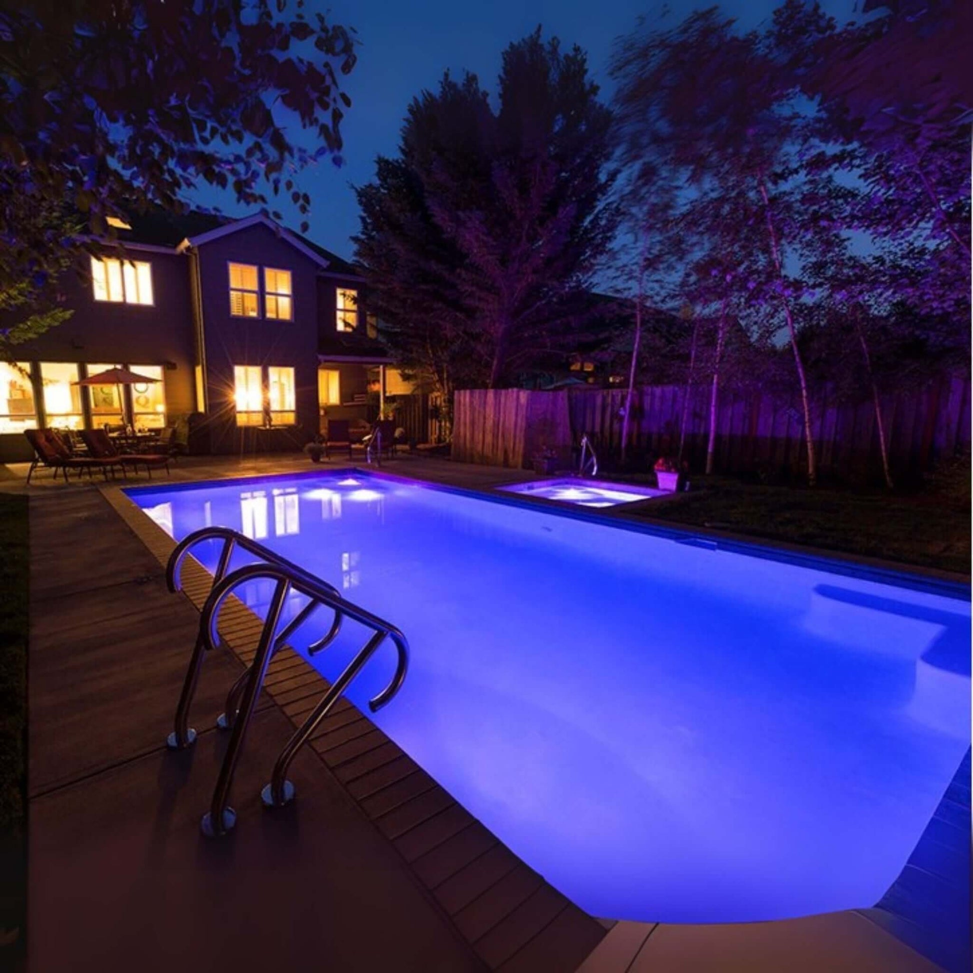 Illuminated swimming pool at night showing vibrant purple lighting, surrounded by a modern backyard.
