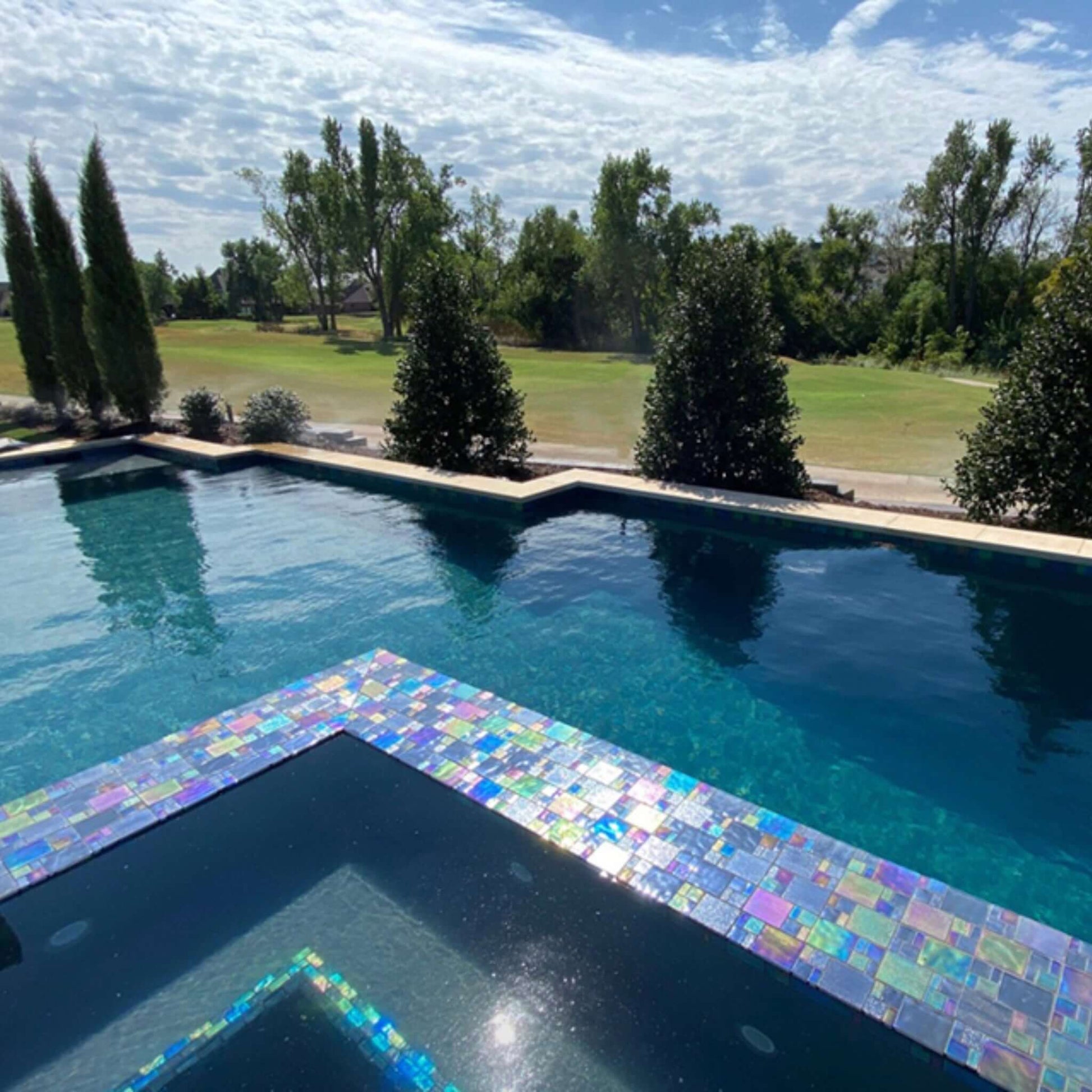 Beautiful pool featuring iridescent mosaic glass tiles in vibrant colors under a clear sky, ideal for outdoor settings.
