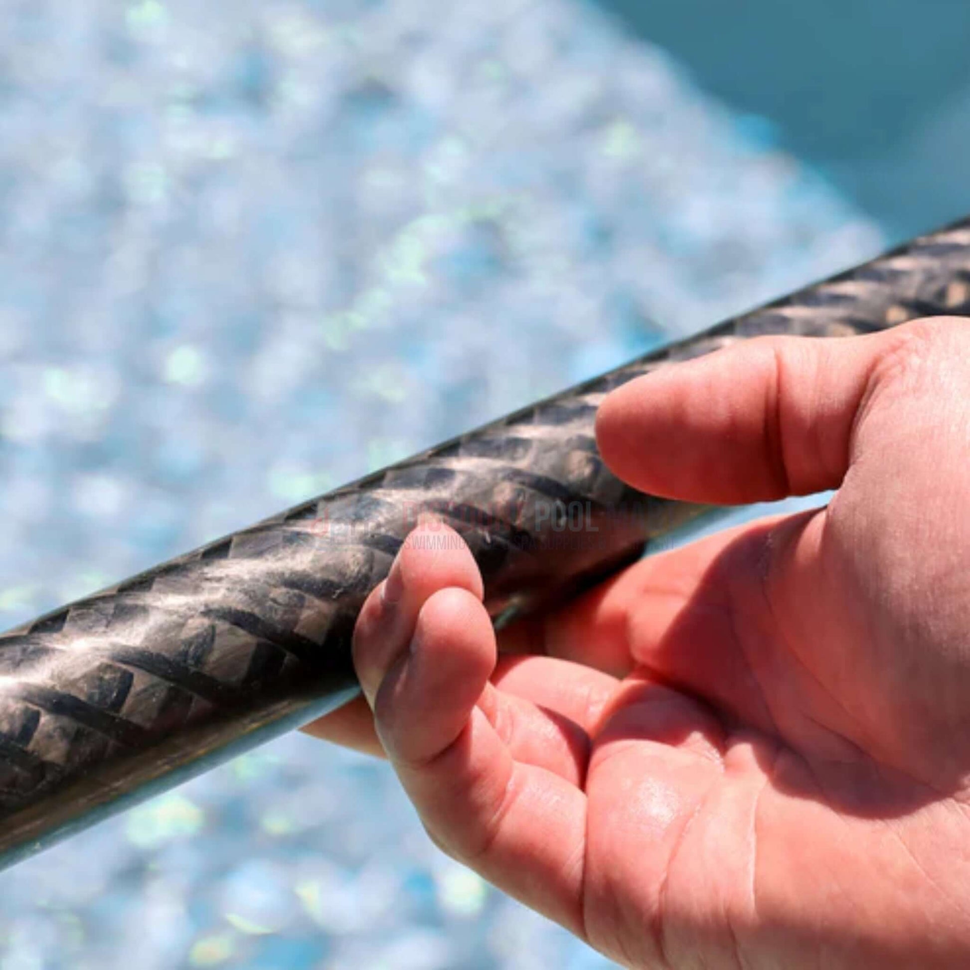 Hand gripping the Skimlite Carbonlite Pool Pole Lever Lock (CL820L) near a swimming pool, showcasing its carbon fiber texture.