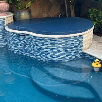 Custom spa and hot tub cover by Discount Pool Mart DPM atop a stone wall, showcasing water reflection and vibrant blue tiles.