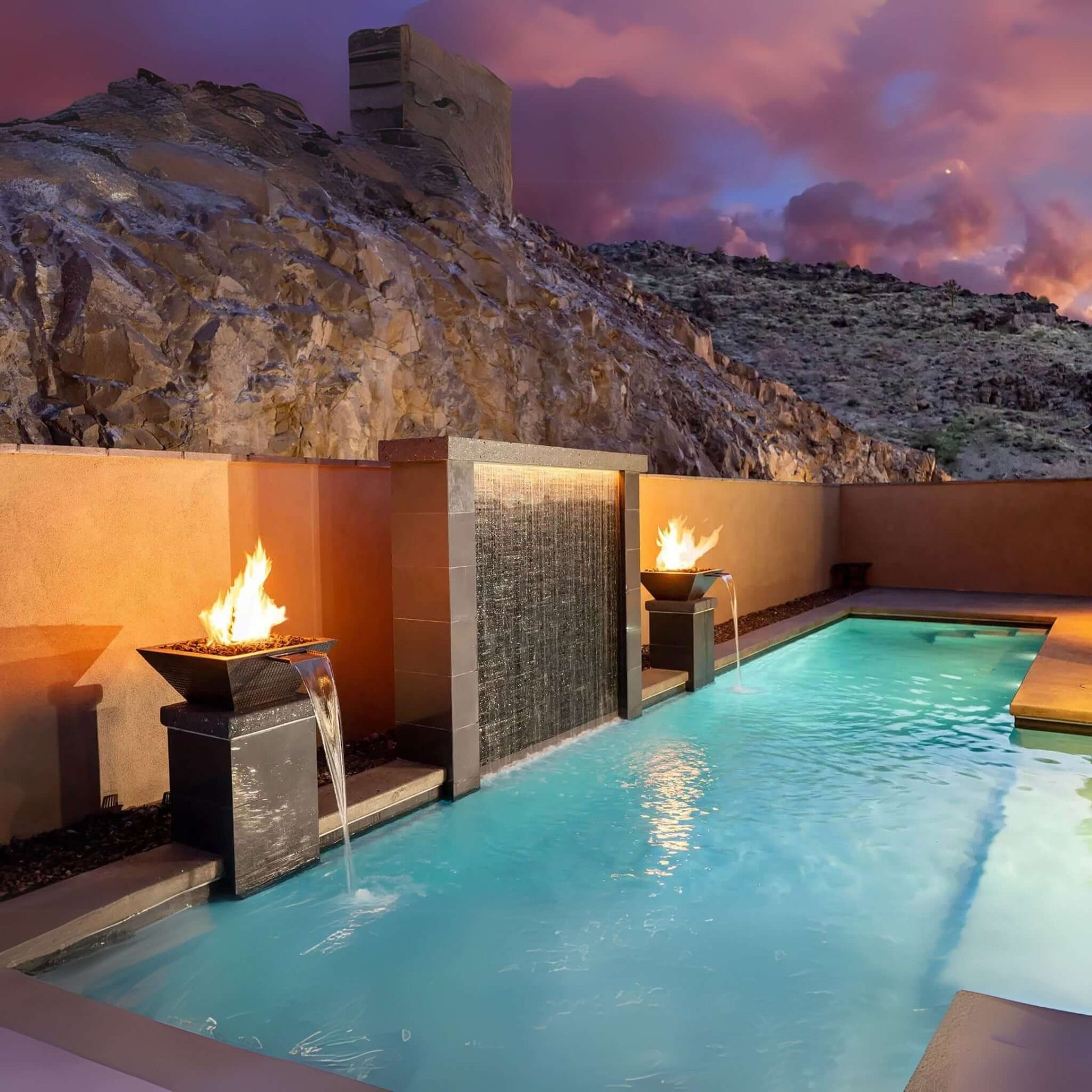Outdoor pool with fire features in a stunning natural landscape, perfect for luxury relaxation. Discount Pool Mart DPM.
