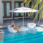 Woman relaxing in TenJam Pool Moon Chairs by the poolside under a sun umbrella. SKU: DPM Splash Series.