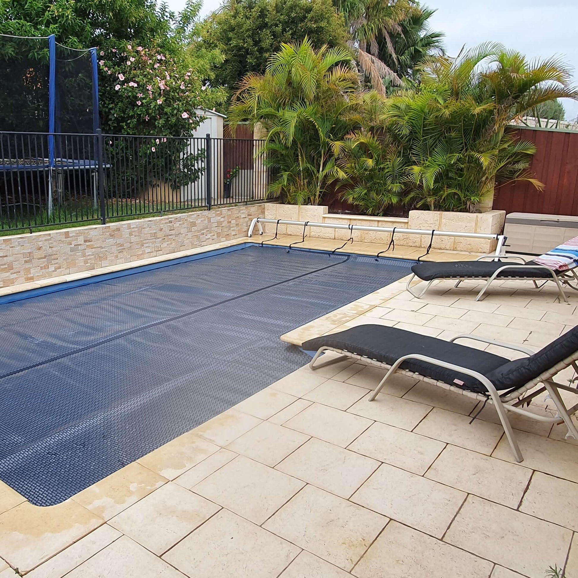 EnergyGuard™ solar pool cover installed neatly on a backyard inground pool, viewed from poolside.